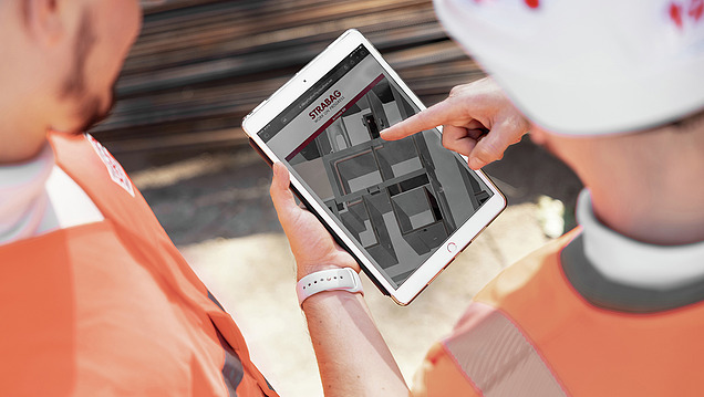 Une photo de dos de deux employés de STRABAG sur un chantier en train de regarder ensemble un modèle BIM sur une tablette.