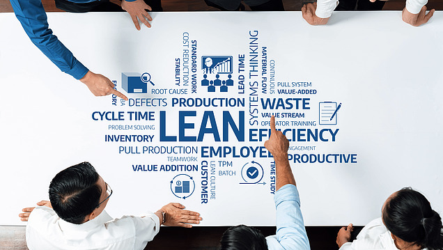 Photo en vue de dessus d'employés regardant un très grand diagramme LEAN sur une table. 