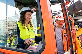 Photo of a UZ Gent employee in an excavator, with a STRABAG-Belgium worker next to her during the groundbreaking ceremony of the new projects at UZ Gent.