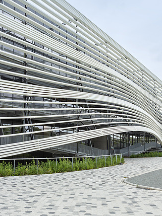 Foto van de golvende gevel van gebouw T HoGent met daarvoor een mooie nieuwe buitenlaanleg. 