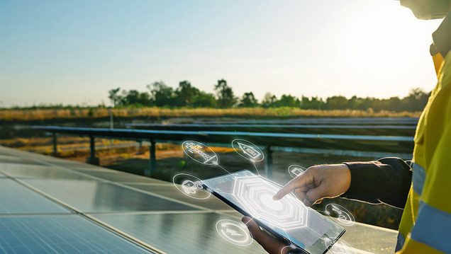 Foto van een medewerker in veiligheidsuitrusting die staat bij zonnepanelen en een tablet bedient.