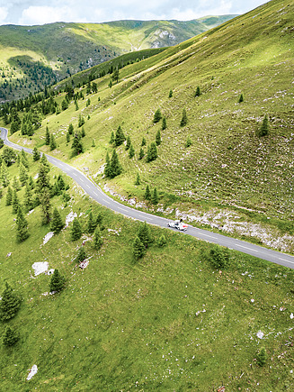 Photo de flancs de montagne verdoyants avec une longue route de circulation. Des pins sont visibles sur les flancs de la montagne.