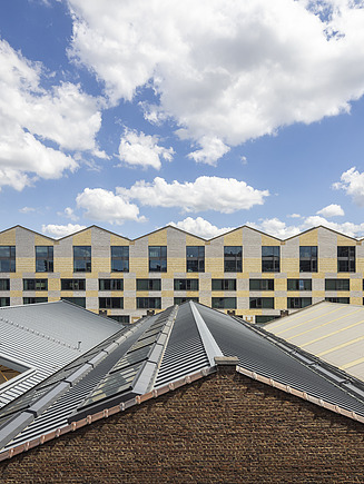 Foto van de sheddaken van de CAd-loodsen met daarachter zicht op het nieuwe Campus Cadix onderwijsgebouw op het Antwerpse eilandnje. 